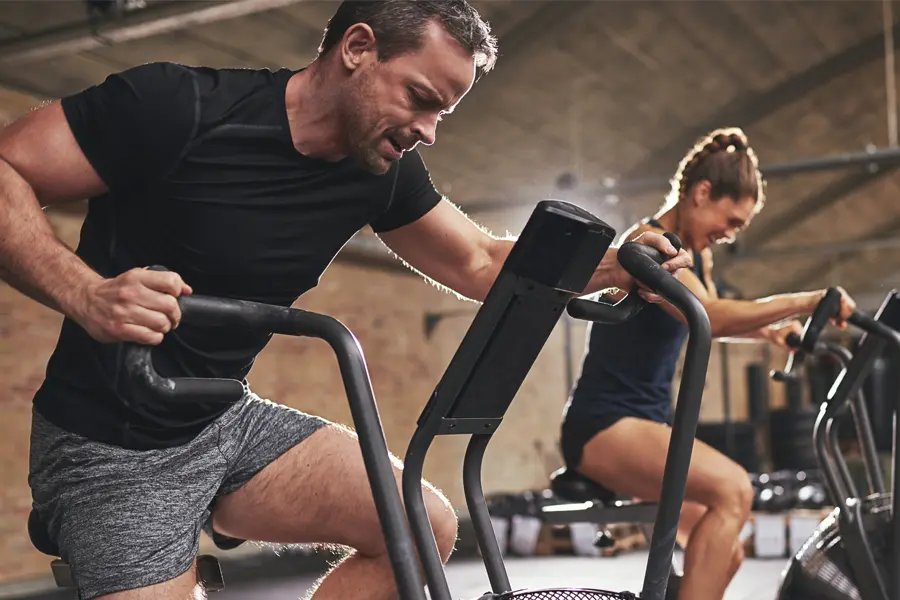 Tirzepatide-Doctor A couple in a brick gym work as hard as they can on exercise bikes, inspired by successful Tirzepatide treatment from Audra Foster, N.D. of Epic Living Medical Center in Pleasanton, California.
